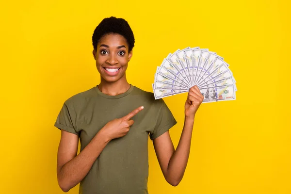 Portrait of cheerful person direct fingers dollars profit look camera isolated on yellow color background.