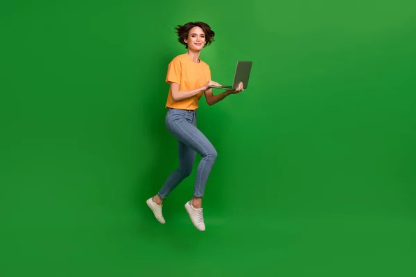 Full body profile photo of attractive lady jump hands hold use wireless netbook isolated on green color background.