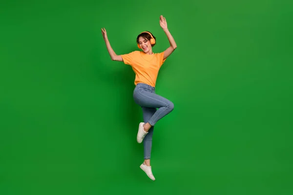 Full body photo of active energetic girl jump enjoy new playlist have good mood isolated on green color background.