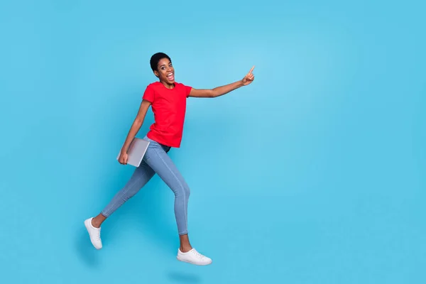 Photo of excited positive short hair human wear red t-shirt jumping running holding device empty space isolated blue color background.