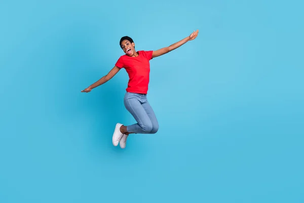 Photo of funky cheerful short hair person dressed red t-shirt jumping high arms sides isolated blue color background.