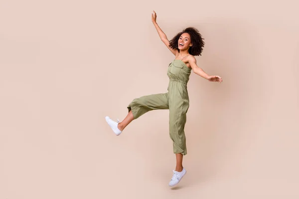 Full length photo of attractive young girl curly hair jumping carefree have fun wear trendy khaki outfit isolated on beige color background.