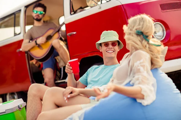 Photo of group carefree people play guitar music sit beanbag drink chatting rest relax pastime outdoors.