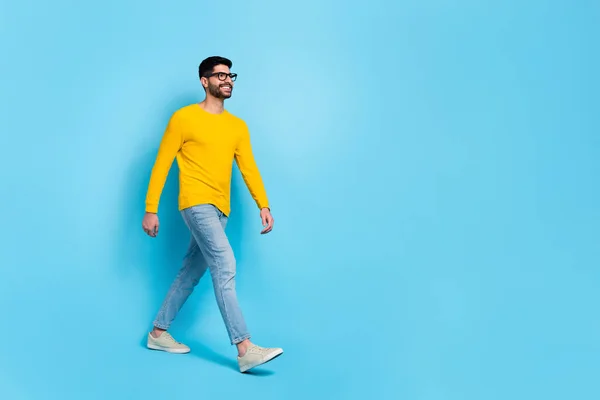 Full body profile photo of cheerful nice young man walking look empty space isolated on blue color background.