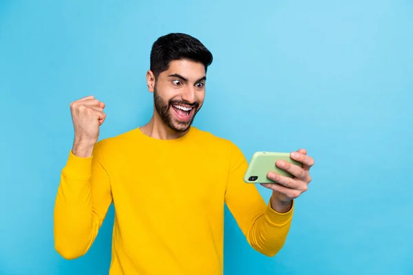 Photo of lucky attractive man wear yellow sweater sport betting modern device empty space isolated blue color background.