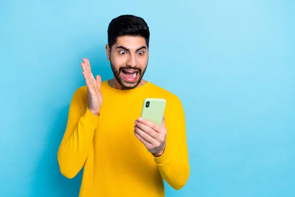 Photo of excited funky man wear yellow sweater reading modern device empty space isolated blue color background.