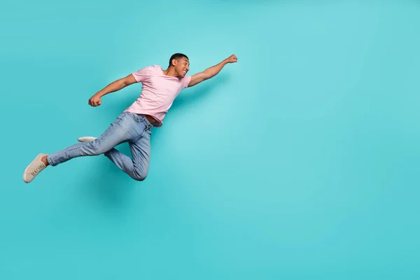 Full length photo of strong hurrying guy wear pink t-shirt jumping high flying help empty space isolated teal color background.