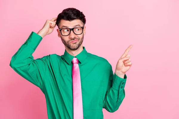 Photo of doubtful unsure man dressed green shirt eyewear finger head pointing empty space isolated pink color background.