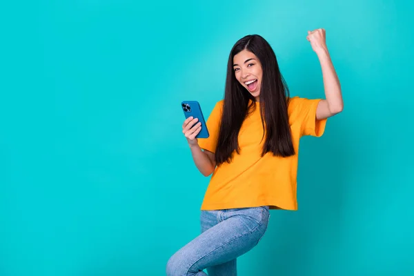 Photo of funky young lady hold telephone hand fist wear orange t-shirt jeans isolated on teal color background.