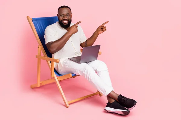 Full body portrait of cheerful man sit chair direct fingers empty space isolated on pink color background.