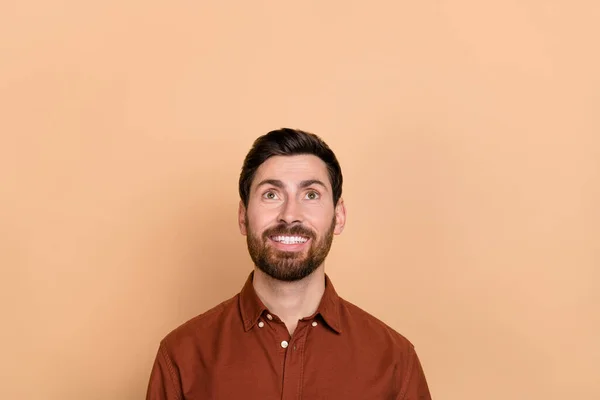 Photo of cheerful satisfied person beaming smile look interested up empty space isolated on beige color background.