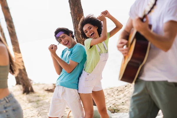 Photo of carefree excited young people enjoy dancing sand beach listen acoustic guitar music outside.