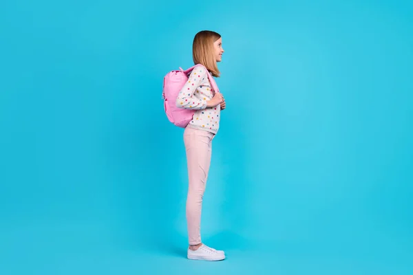 Full length photo of shiny charming small girl wear dotted shirt backpack looking empty space isolated blue color background.