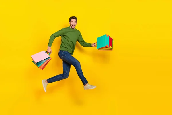 Photo of sweet pretty guy wear green sweater jumping running holding shoppers empty space isolated yellow color background.