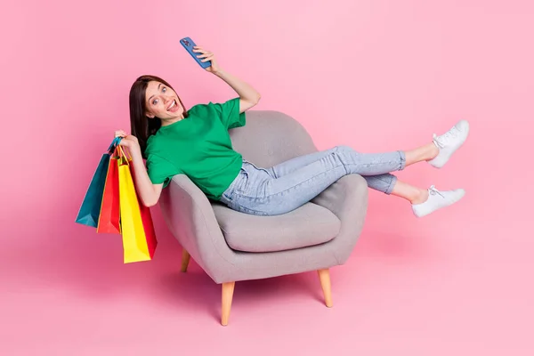 Full body portrait of excited funny lady sit chair hold telephone packages isolated on pink color background.