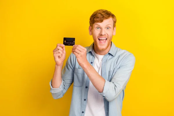 Photo of positive man impressed reaction unbelievable arm hold present credit card empty space isolated on yellow color background.