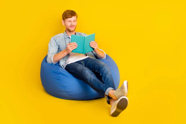 Photo of sweet pretty guy dressed denim shirt sitting bean bag enjoying new story empty space isolated yellow color background.