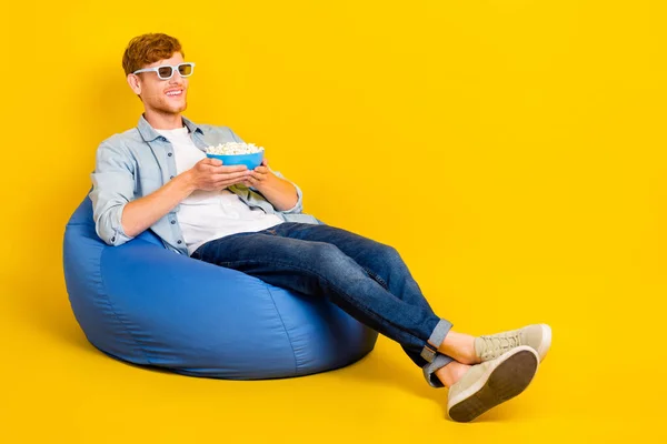 Photo of excited pretty guy dressed denim shirt sitting bean bag enjoying 3d movie empty space isolated yellow color background.