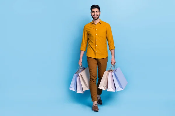 Full body portrait of nice cheerful person arms hold packages walking isolated on blue color background.