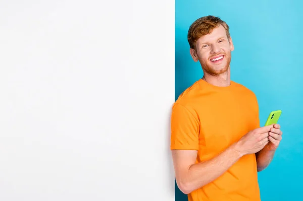 Photo of funky ginger hair guy near telephone wear orange t-shirt isolated on blue color background.