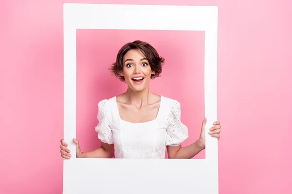 Photo of excited impressed lady wear white blouse looking inside photo frame isolated pink color background.