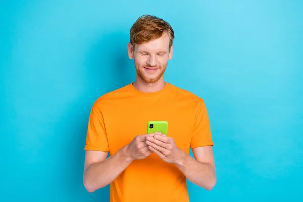 Portrait of positive handsome guy dressed orange t-shirt write comment instagram twitter facebook isolated on turquoise color background.