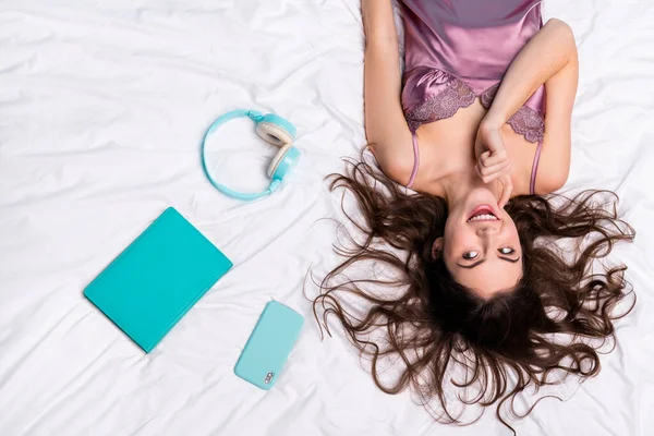 Top above high angle view portrait of beautiful trendy minded cheerful girl choosing device lying on bed linen home.