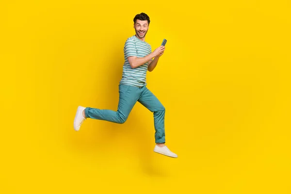 Full body profile photo of funky guy run write telephone wear t-shirt jeans boots isolated on yellow color background.