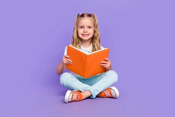 Full body photo of charming little girl tails sit crossed legs read book dressed stylish white clothes isolated on violet color background.