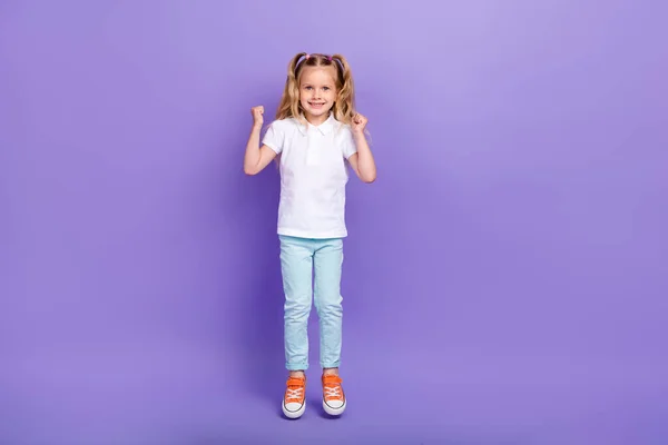 Full length photo of cute small girl tails raise fists jump win competition wear stylish white blouse isolated on violet color background.