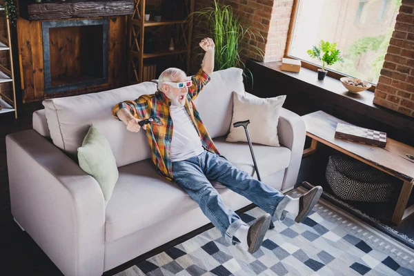 Photo of lucky funky retired man dressed plaid shirt 3d glasses watching movie sitting couch indoors apartment.