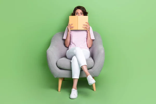 Photo of impressed lady sit cozy chair hide face look read mystery detectives interesting scary plot isolated on green color background.