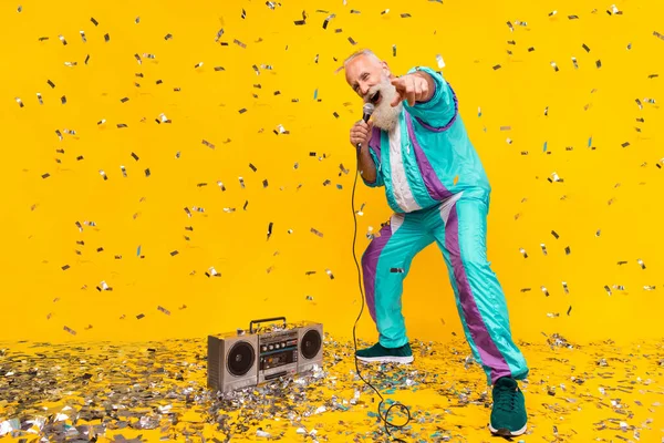 Full body portrait of overjoyed funky granddad hand hold microphone point finger you isolated on yellow color background.