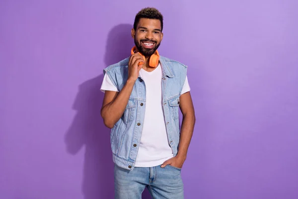 Photo of cool positive guy dressed denim vest earphones smiling empty space isolated purple color background.