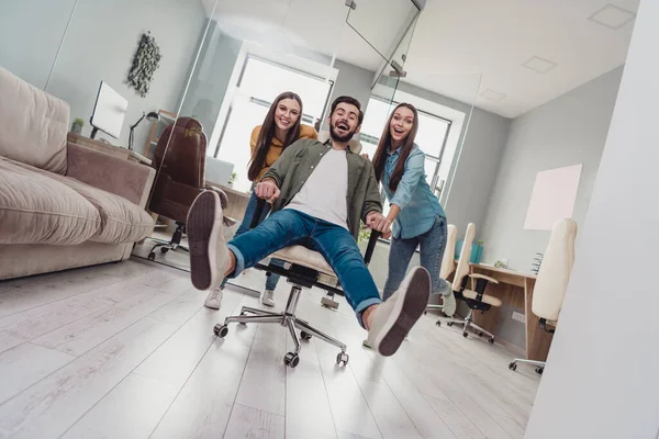Full body photo of three childish employees push chair ride fast speed office indoors.