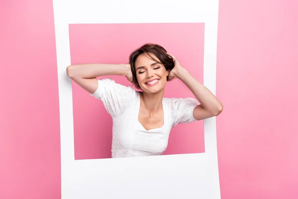 Photo of dreamy adorable lady wear white blouse arms hair looking inside photo frame isolated pink color background.