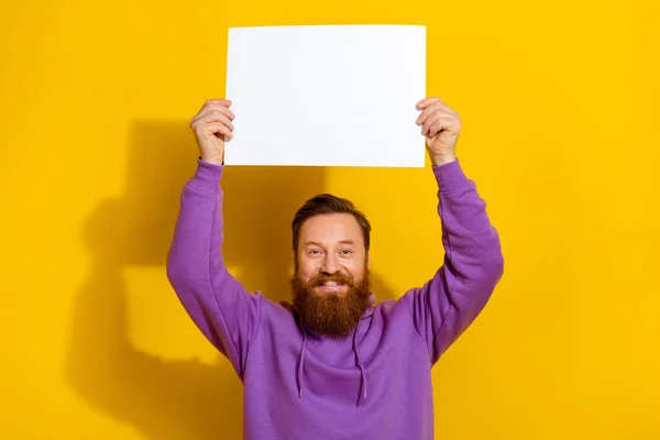 Portrait of cheerful excited person arms hold empty space paper above head isolated on yellow color background.