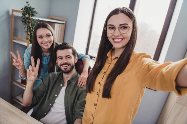 Photo of cheerful partners company smiling taking selfie showing v-signs indoors workstation workshop.