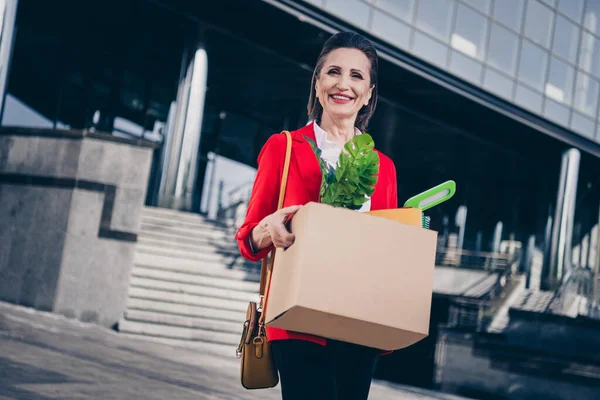 Photo of aged lady marketer hold cardboard package change workplace feel optimistic opportunity outdoors.