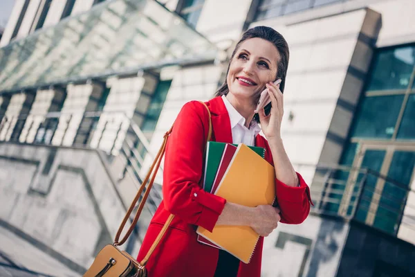 Photo of pretty positive senior assistant woman dressed red blazer communicating modern gadget outdoors urban town street.