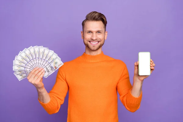 Photo of good mood man show you giveaway present choose between phone and money isolated on violet color background.