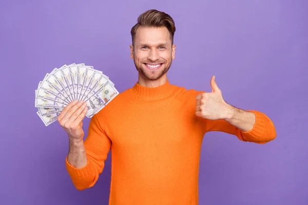 Photo of cheerful man win money prize lottery showing thumb-up wear knitted pullover isolated on violet color background.