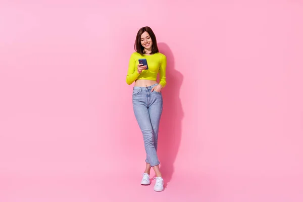 Full length photo of pretty cute girl dressed lime shirt walking chatting modern device isolated pink color background.