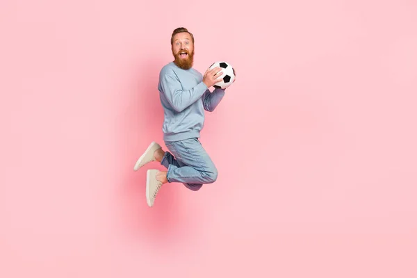 Full body photo of excited satisfied person jumping hands hold football isolated on pink color background.