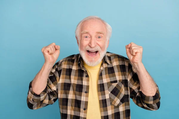 Photo of excited lucky man pensioner dressed checkered shirt rising fists isolated blue color background.