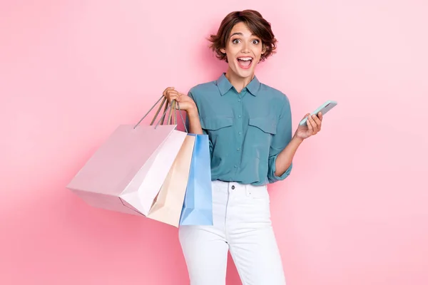 Portrait photo of young crazy amazed woman wear blue shirt shocked hold phone package online shopping delivery isolated on pink color background.