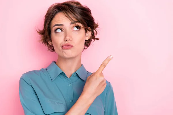 Closeup photo of young pretty adorable gorgeous funny woman wear blue shirt pouted lips uncertain about this sale finger directing empty space isolated on pink color background.