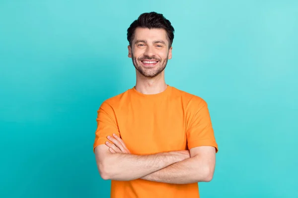 Portrait photo of young successful positive good mood man wear orange t-shirt crossed arms rich programmer boss leader isolated on aquamarine color background.