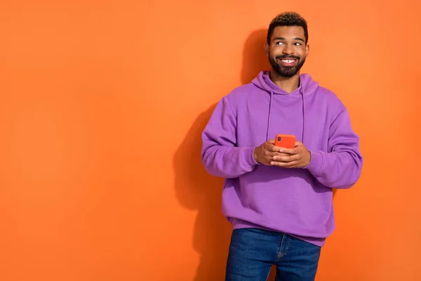 Photo of attractive guy wear purple clothes buy at discounts modern device look empty space enjoy isolated on orange color background.