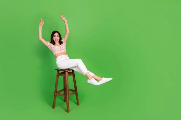 Photo of impressed funky lady wear print top rising arms sitting bar chair empty space isolated green color background.